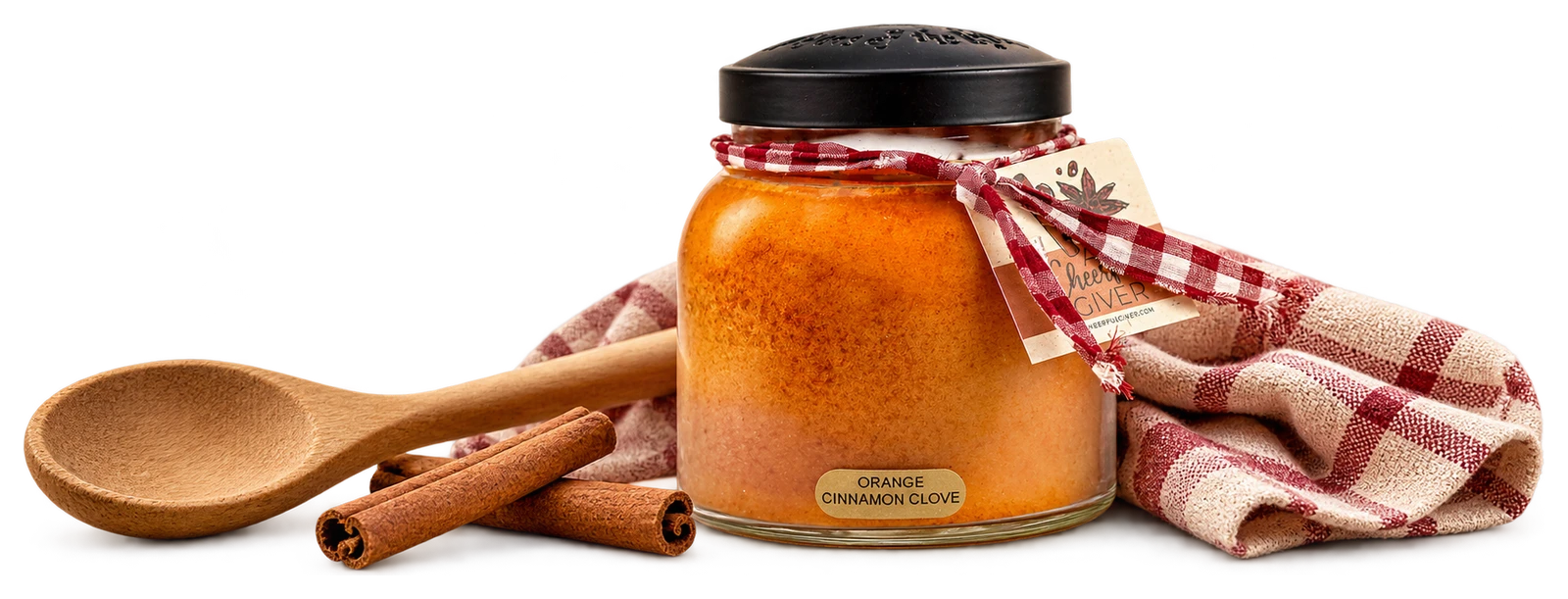 The actual orange Papa jar candle beside an unused wooden spoon, cinnamon and a checked kitchen cloth.